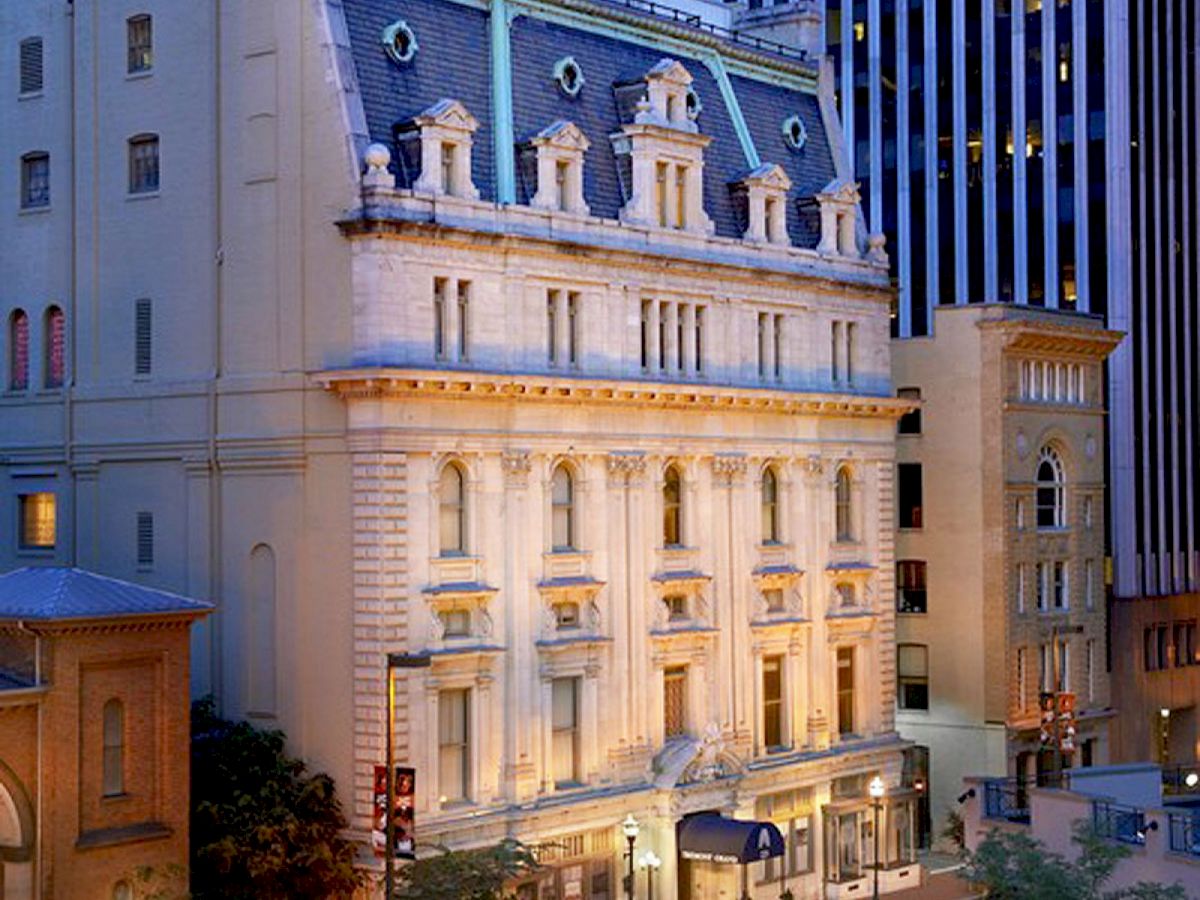 A historic building with classic architecture, nestled between modern skyscrapers in a city environment, illuminated by street lights in the evening.