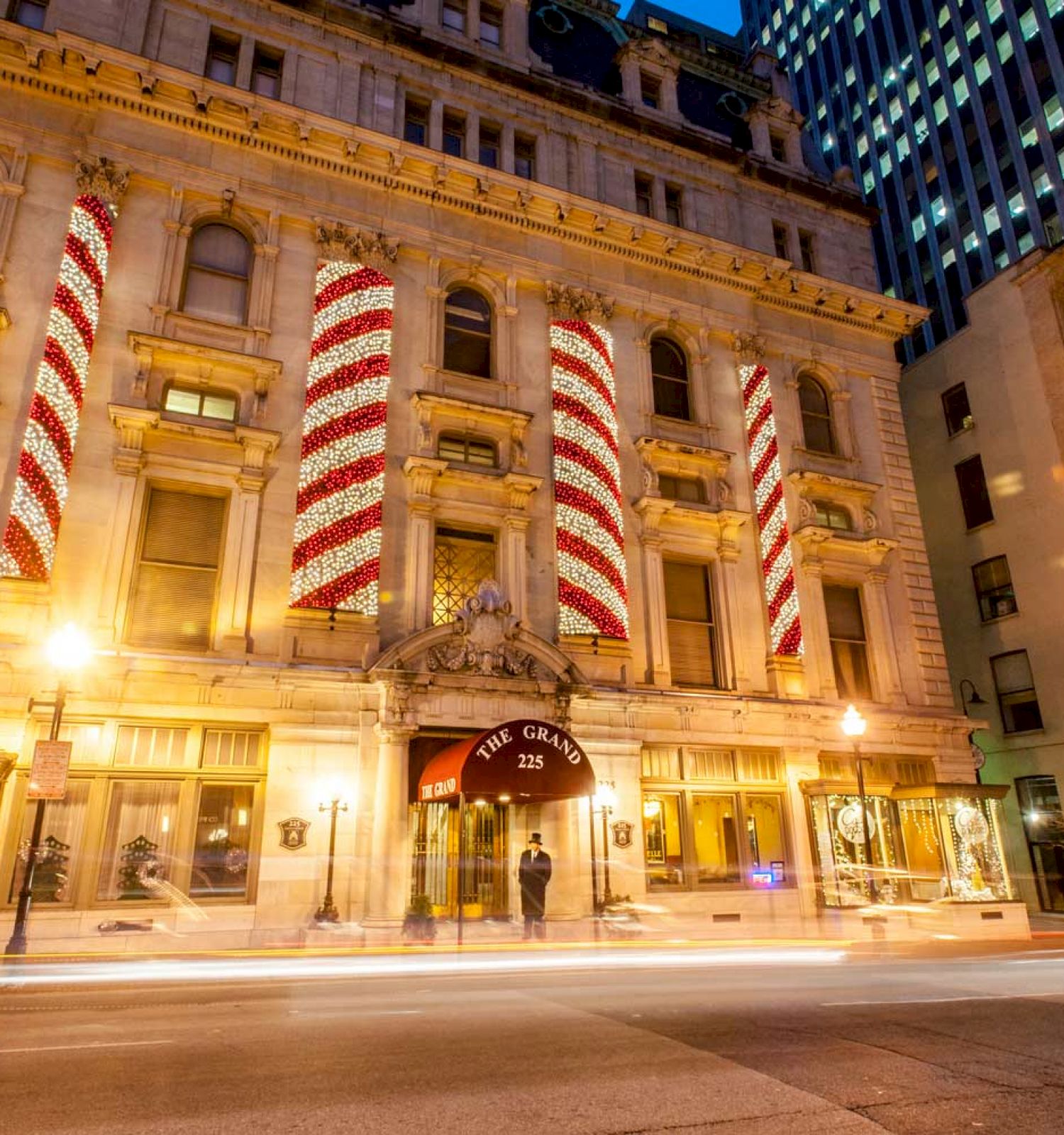 The image shows a historic building with large red and white ribbons hanging between its windows, illuminated by streetlights, and blurred car lights passing by.