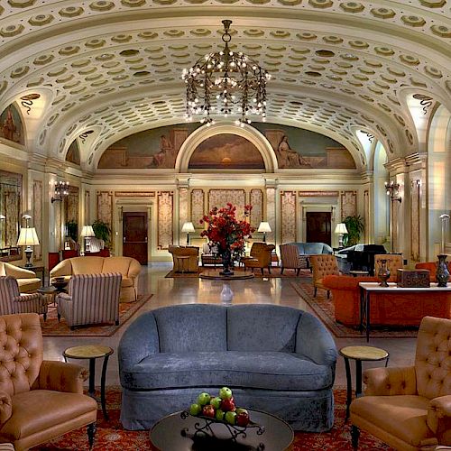 Elegant, opulent lobby with chandeliers, ornate ceiling, plush seating, and elaborate decor. Symmetrical layout with a central table of flowers ending the sentence.