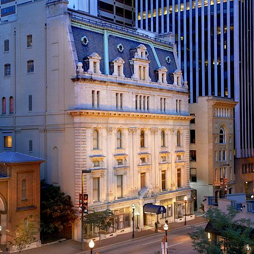 An elegant building with ornate architecture and a fancy facade, surrounded by taller modern structures in an urban setting.