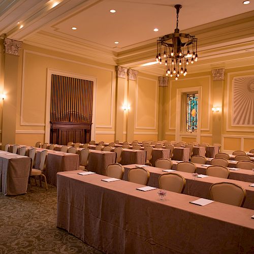 This image shows an elegant conference room setup with rows of tables and chairs, notepads on tables, chandeliers, and stained glass windows.