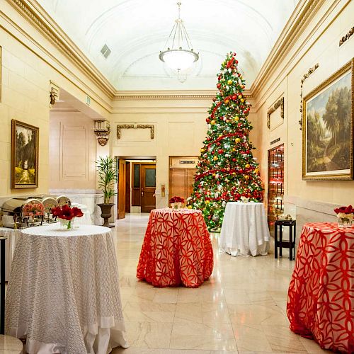 A decorated hallway with a Christmas tree, round tables with red and white tablecloths, and festive decor. There is a sign reading 