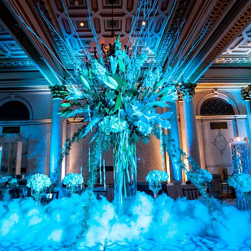 An opulent indoor venue illuminated with blue lighting features extravagant floral arrangements and decorative elements, creating a luxurious ambiance.