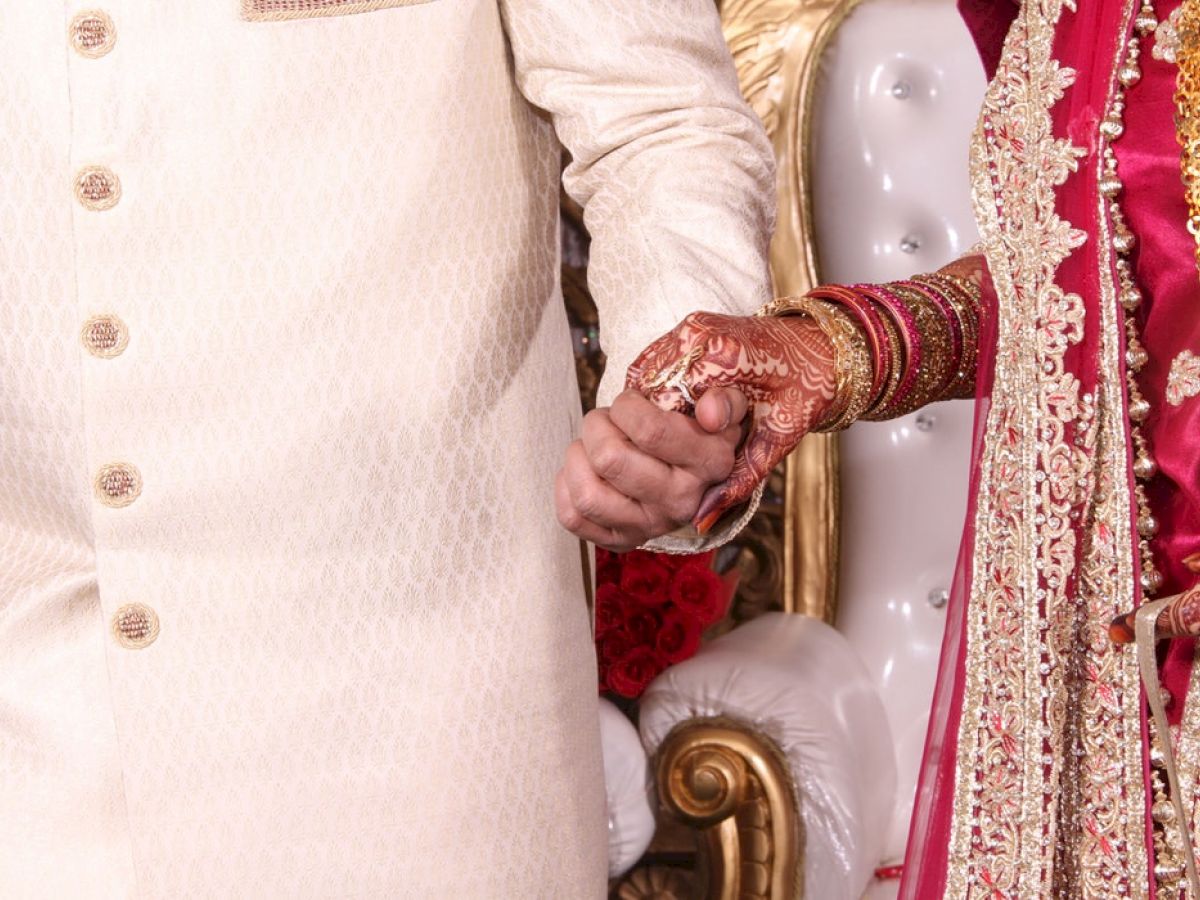 A couple dressed in traditional attire holding hands, likely at a wedding or related celebration, featuring henna and intricate outfits.