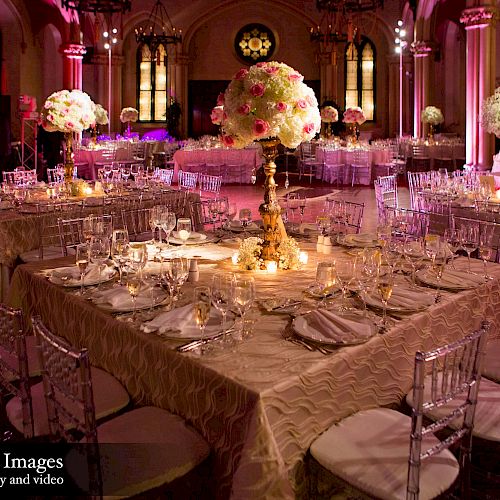 The image shows an elegant event setup with decorated tables, floral centerpieces, and fine dining ware in a dimly lit venue.