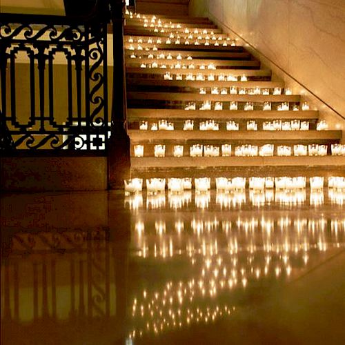 A staircase is lined with numerous candles, creating a warm and inviting atmosphere, reflecting light beautifully on the polished floor.