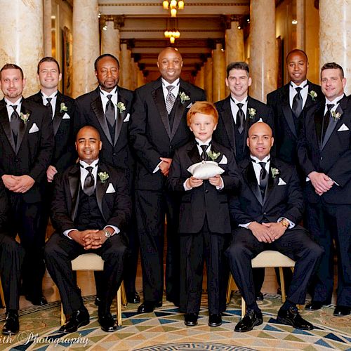 A group of men in formal suits, likely a wedding party, posing for a photo in an elegant hallway.