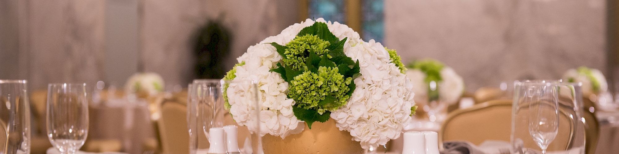 A beautifully set table features a floral centerpiece in a gold vase, surrounded by elegant glassware and cutlery in an ornate dining room.