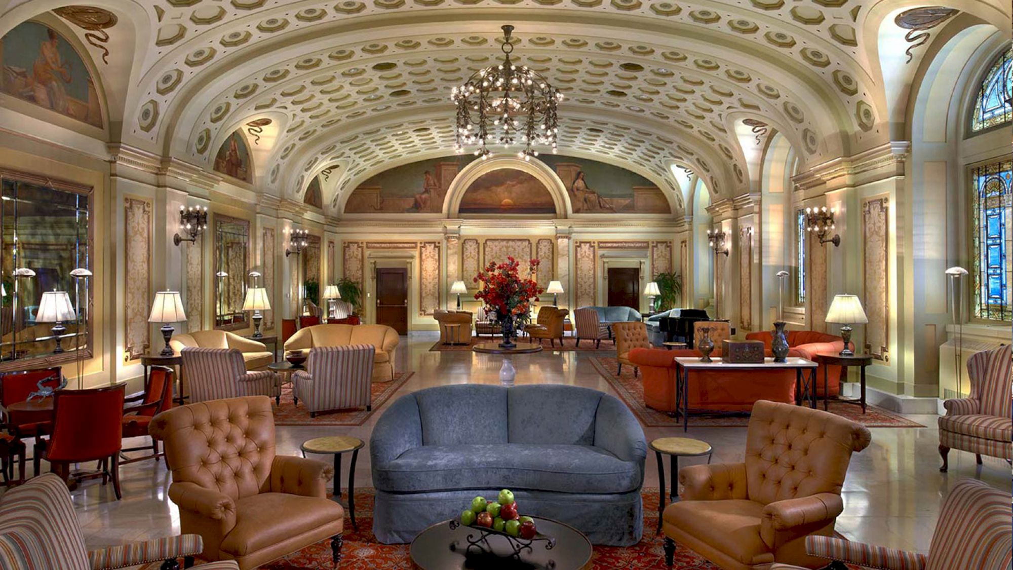 A luxurious, ornate hotel lobby with elegant furniture, chandeliers, and high ceilings. The room features a blend of classic and modern decor elements.