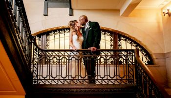 A couple is sharing a kiss on an ornate staircase in a beautifully lit setting, captured by Rachel Smith Photography.