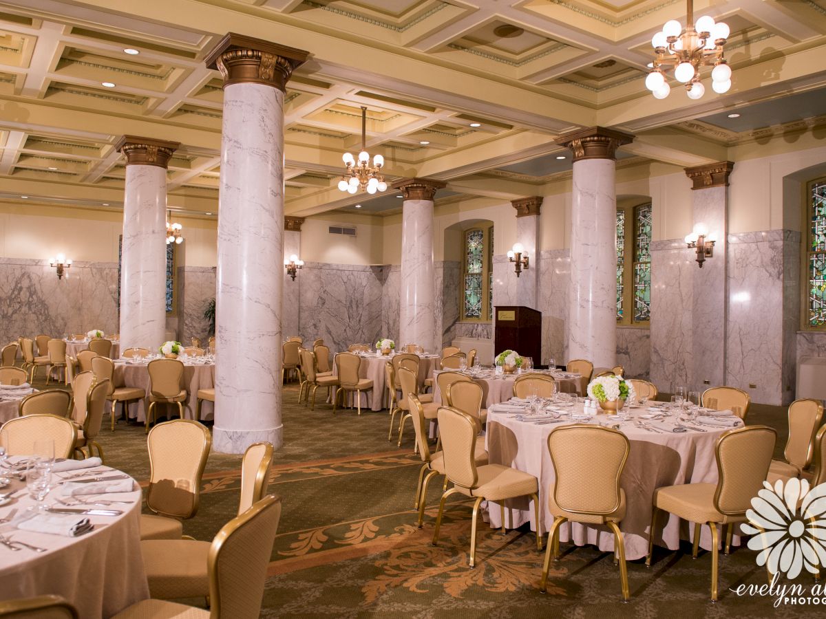 A beautifully decorated banquet hall with round tables covered in white linens and floral centerpieces, ready for an event.